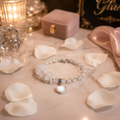 Crystal Bloom Heart Charm Bracelet laid on an elegant vanity surrounded by white flower petals by Be Glitzy Glam